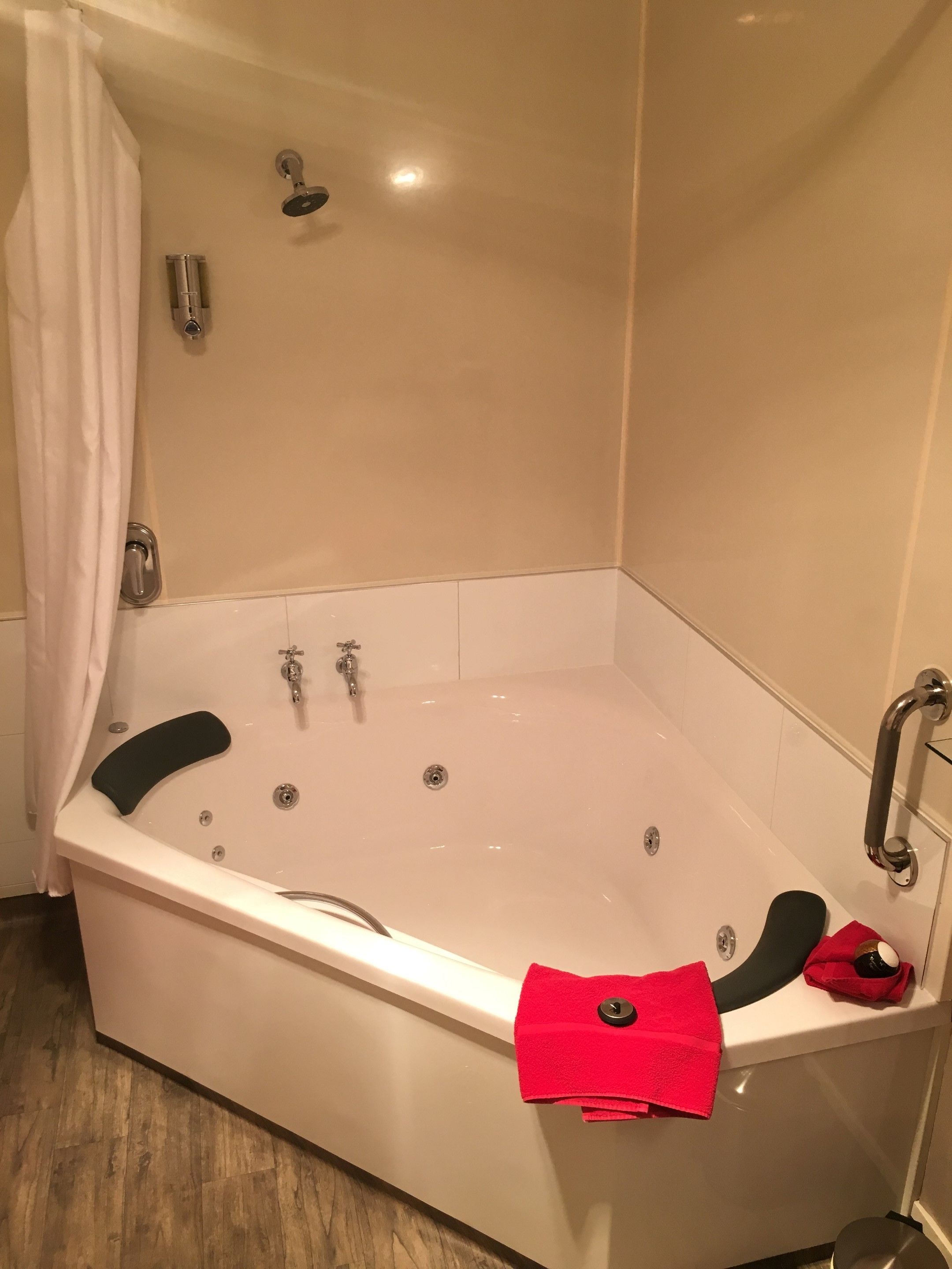 A corner bathtub with a showerhead, a handheld shower, and a handheld shower attachment.