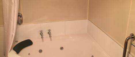 A corner bathtub with a showerhead, a handheld shower, and a handheld shower attachment.