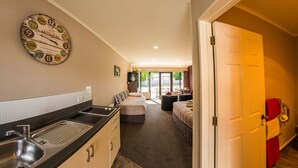 Habitación de hotel compacta con kitchenette, cama, zona de estar y puerta a un balcón.