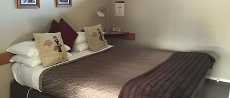 Una cama bien hecha con ropa de cama estampada, una lámpara de noche y un pequeño estante con un teléfono.