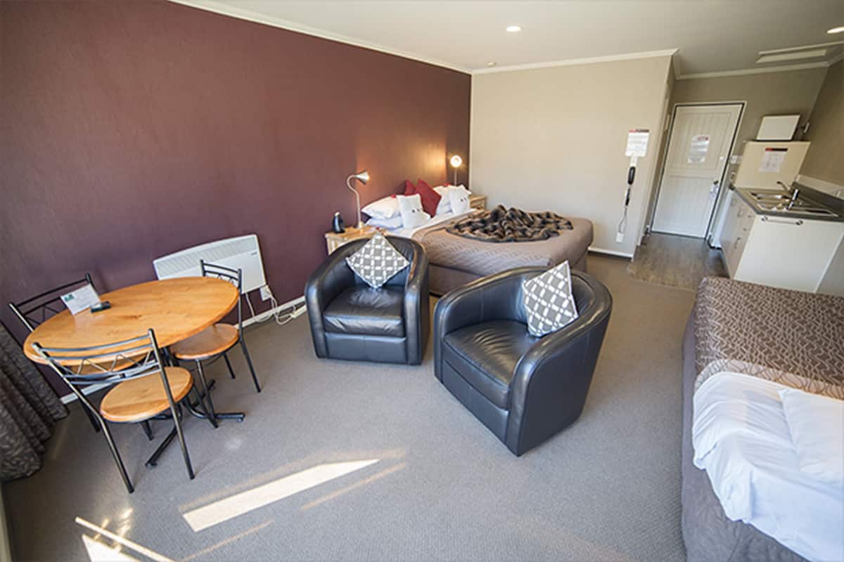 Habitación de hotel con una cama, dos sillones de cuero, una mesa de madera, un escritorio y una kitchenette.