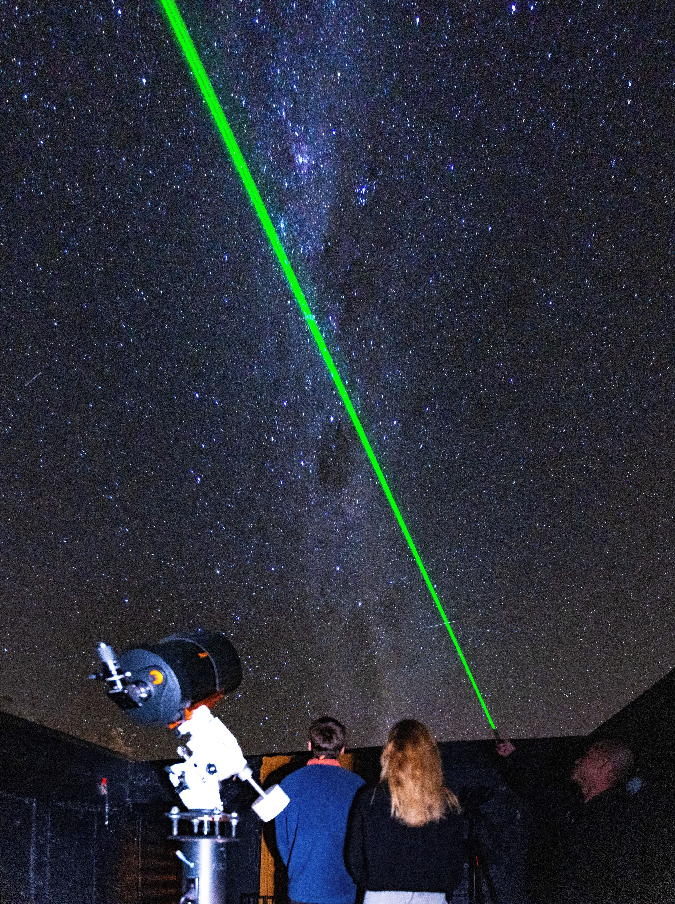 A telescope with a green laser beam pointing at the stars, indicating a stargazing event.