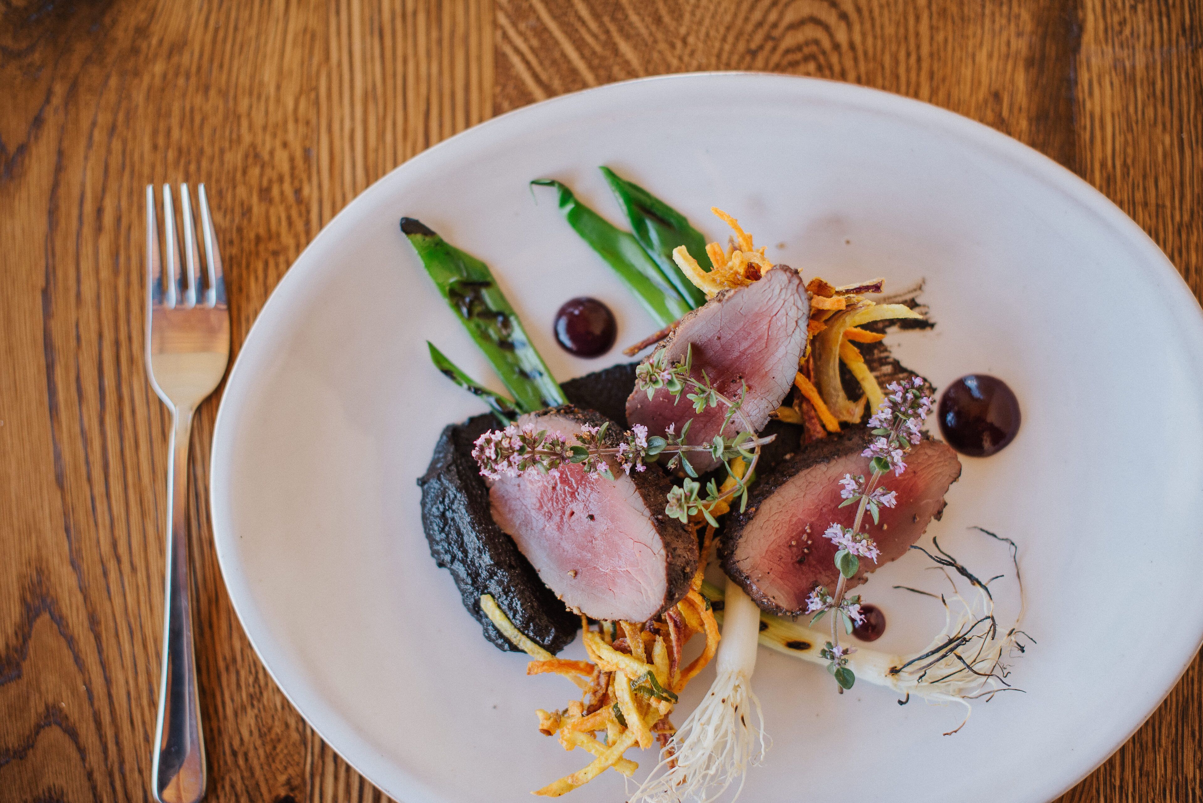 A plate of food with asparagus, a fork, and a wooden table.