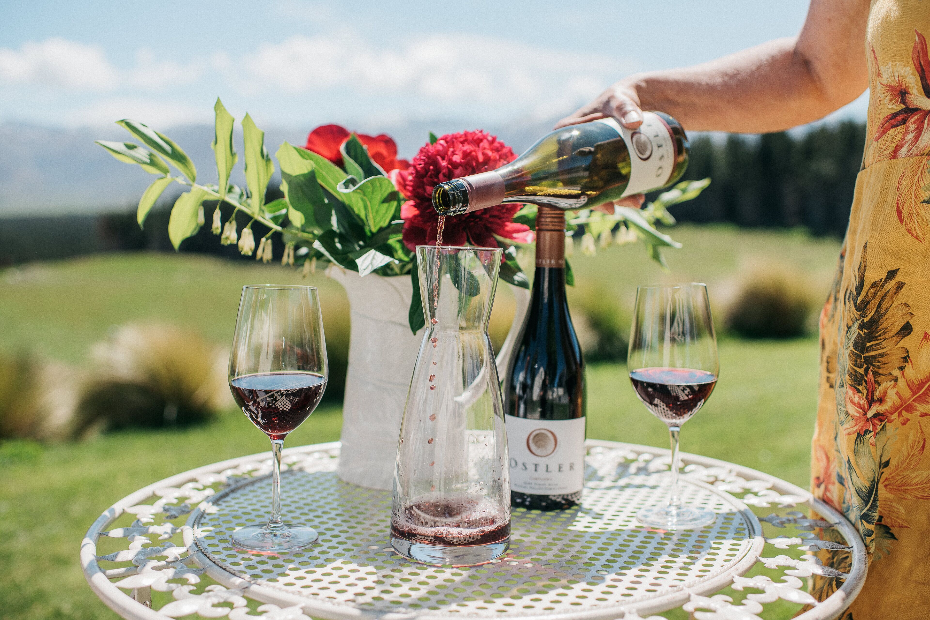A table with a bottle of wine and two glasses on a white metal table with a floral pattern.