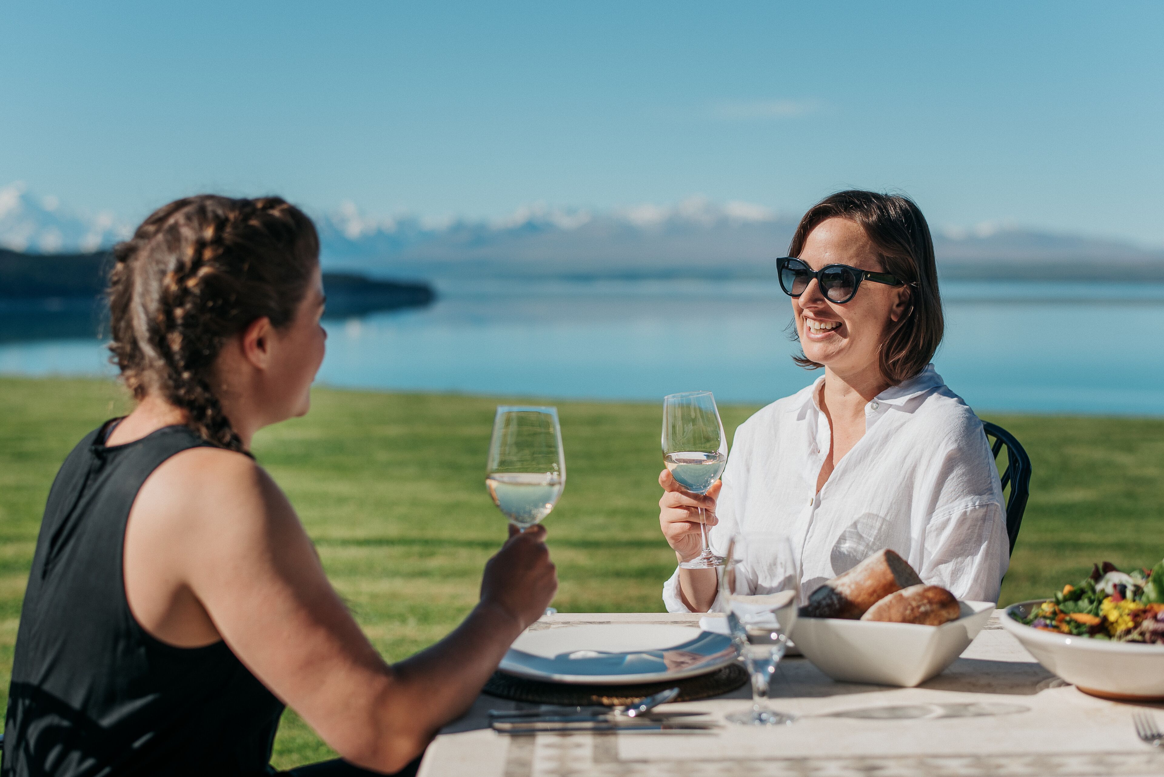 Two people dining outdoors with a table set for a meal, a bowl of salad, and a plate of bread.