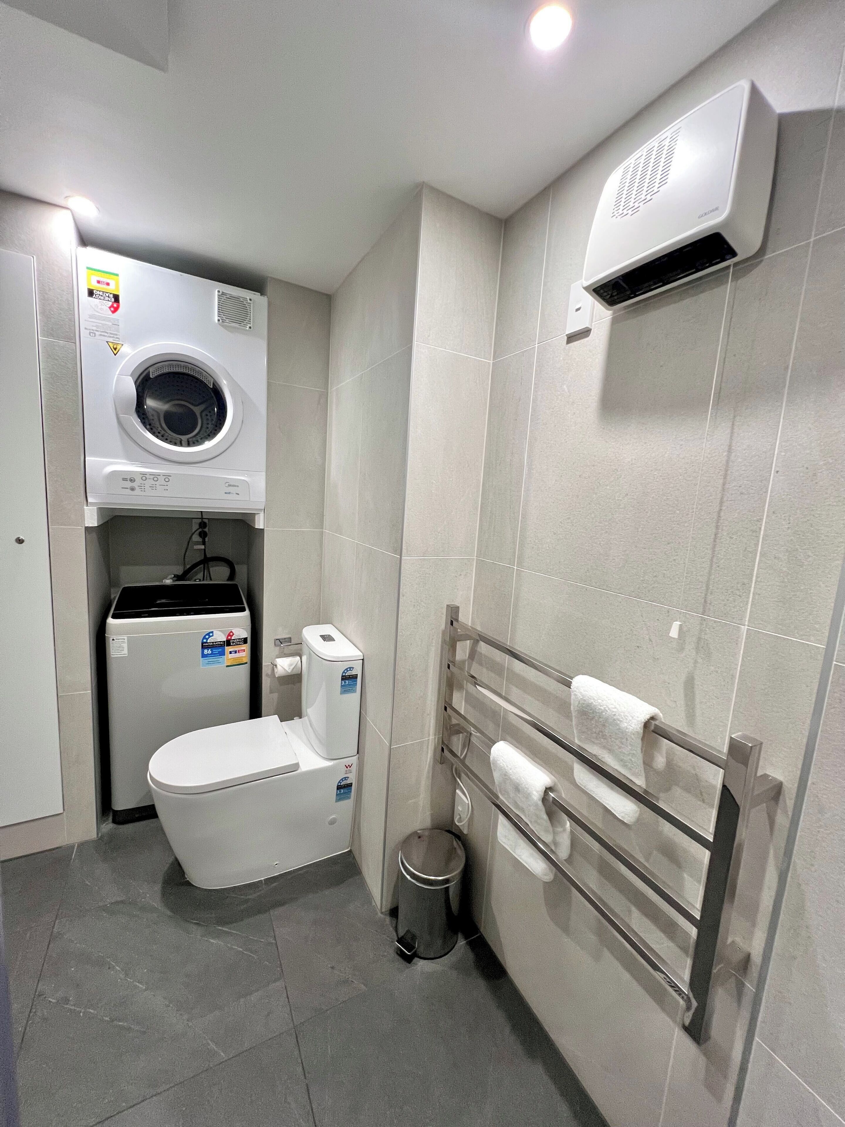 Un bagno piccolo con il water, una lavatrice, un cestino e un porta asciugamani.