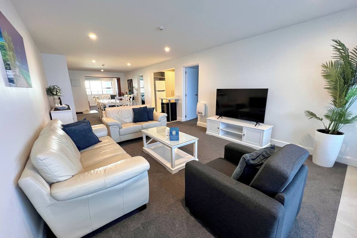 A modern living room with a white sofa, a dark armchair, a coffee table, and a TV on a white stand.