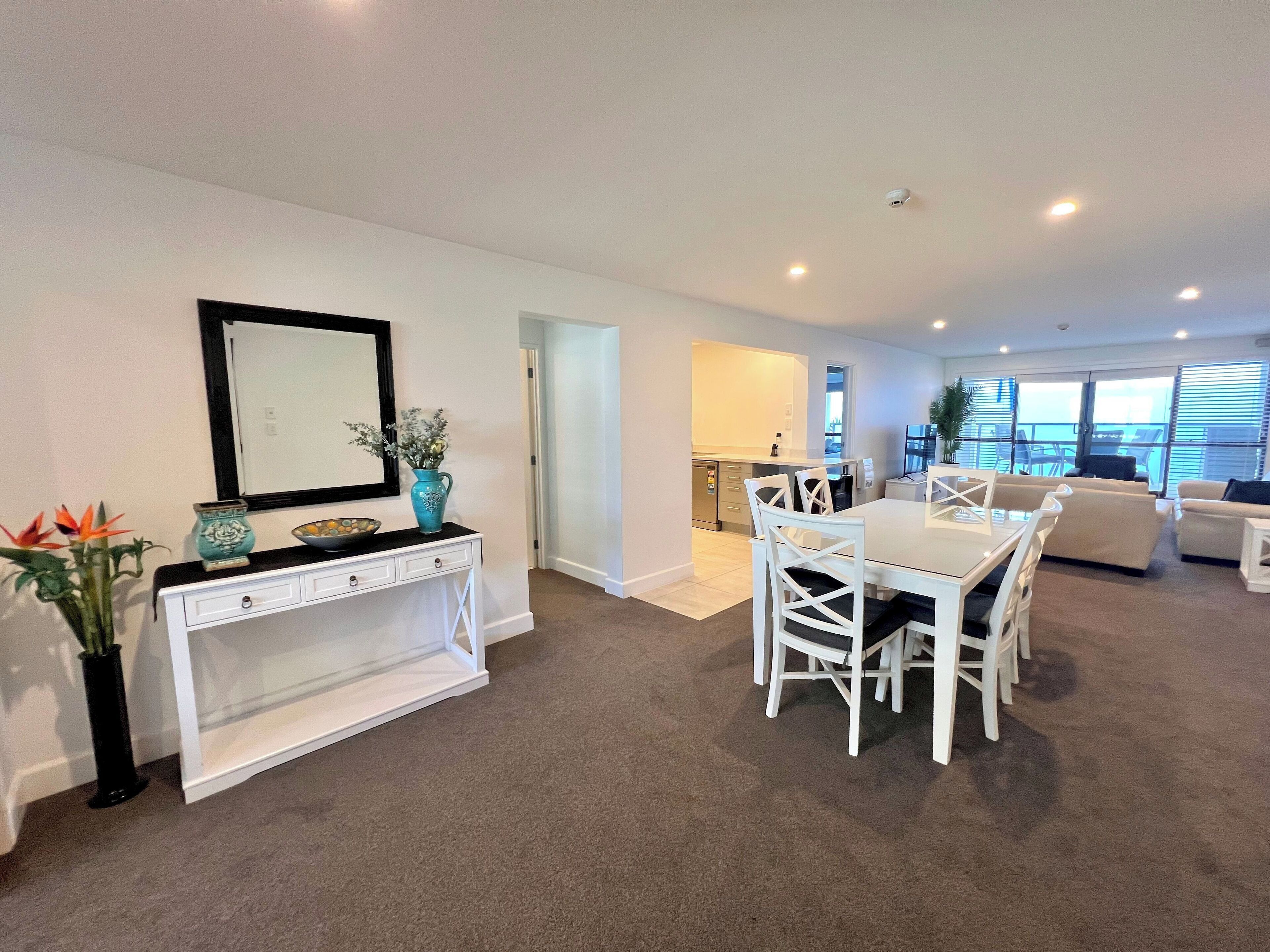 A modern living room with a dining area, white furniture, and a view of the balcony.