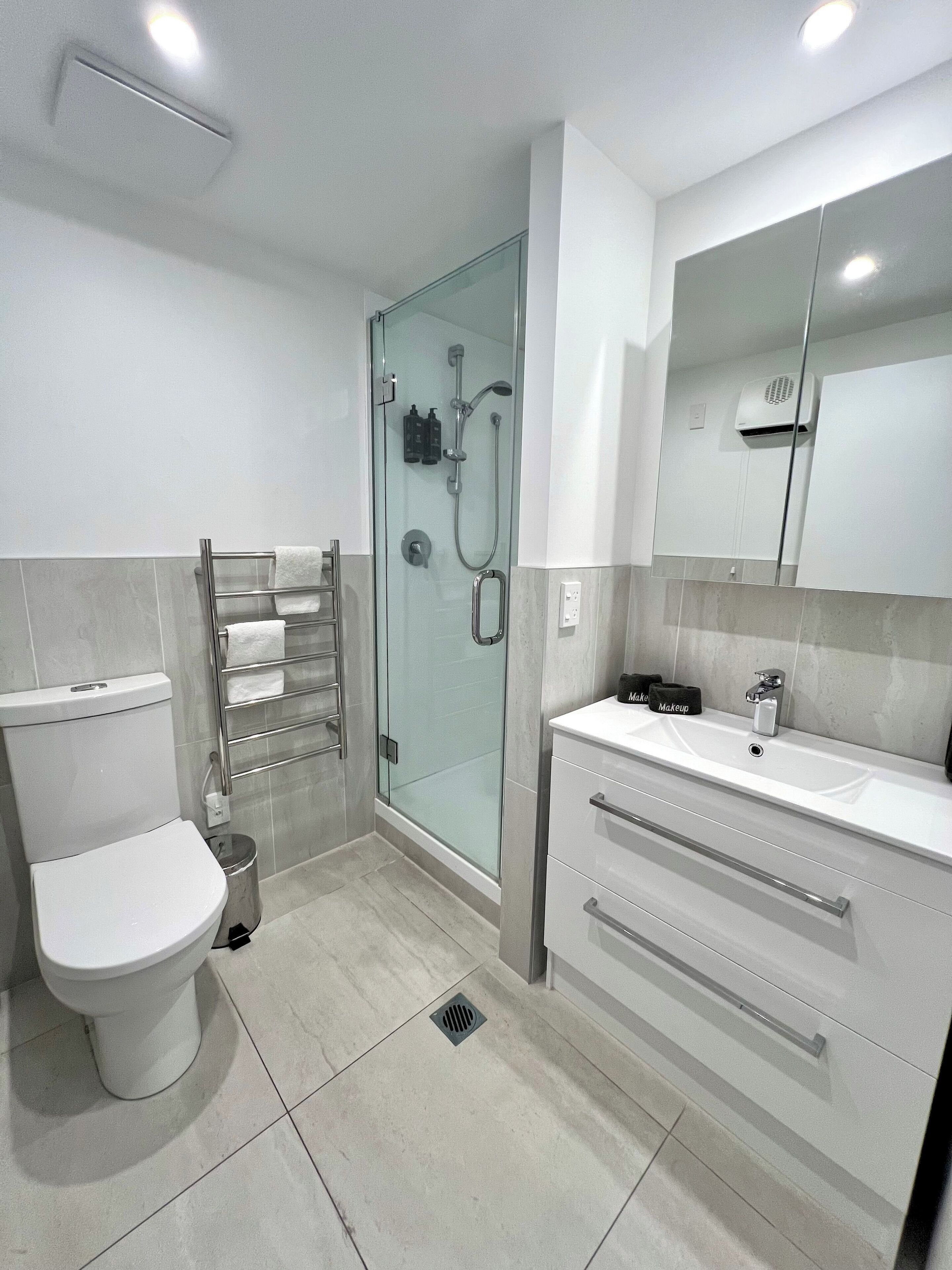 Un baño moderno con inodoro, ducha con cerramiento de vidrio y tocador con espejo.