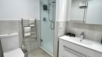 Un baño moderno con inodoro, ducha con cerramiento de vidrio y tocador con espejo.