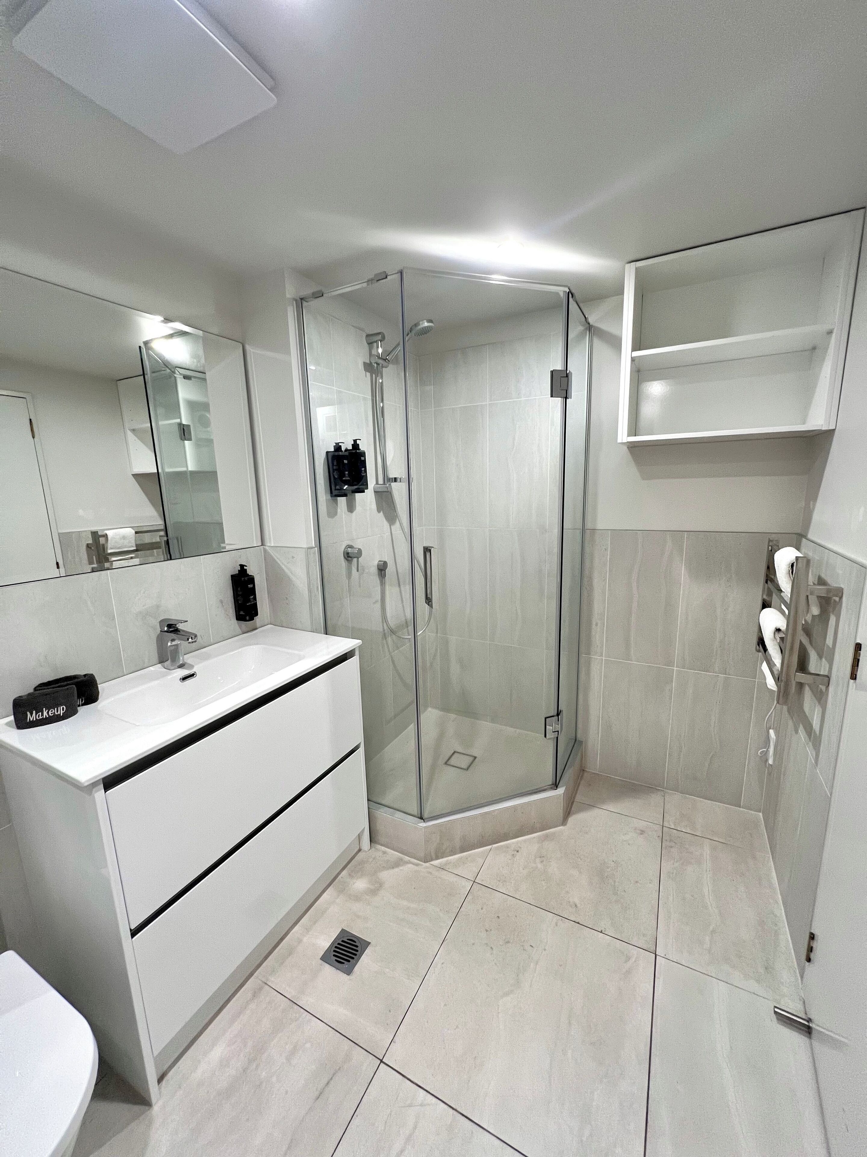 A modern bathroom with a glass-enclosed shower, a white vanity with a mirror, and a tiled floor.