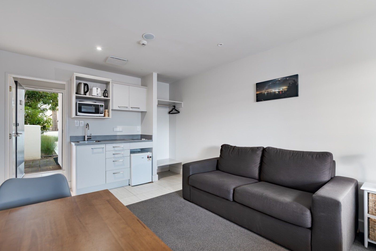 A compact living space with a kitchenette, a grey sofa, and a dining table.