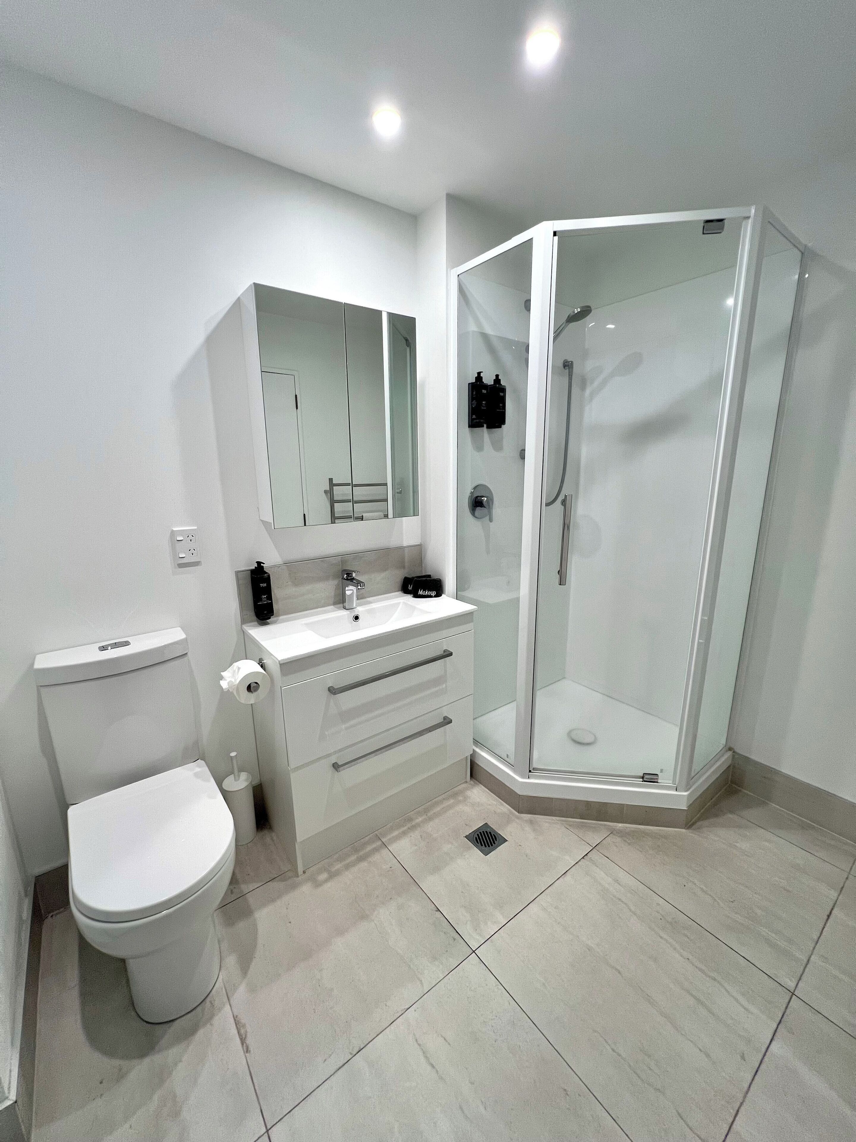 A modern bathroom with a toilet, sink, mirror, and glass-enclosed shower.