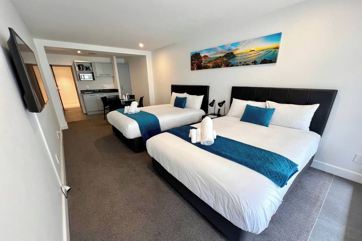 A hotel room with two beds, a painting, and a kitchenette.