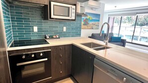 A modern kitchen with dark wooden cabinets, a stainless steel microwave, a built-in oven, and a dishwasher. - 6 on Adams  (Tauranga)