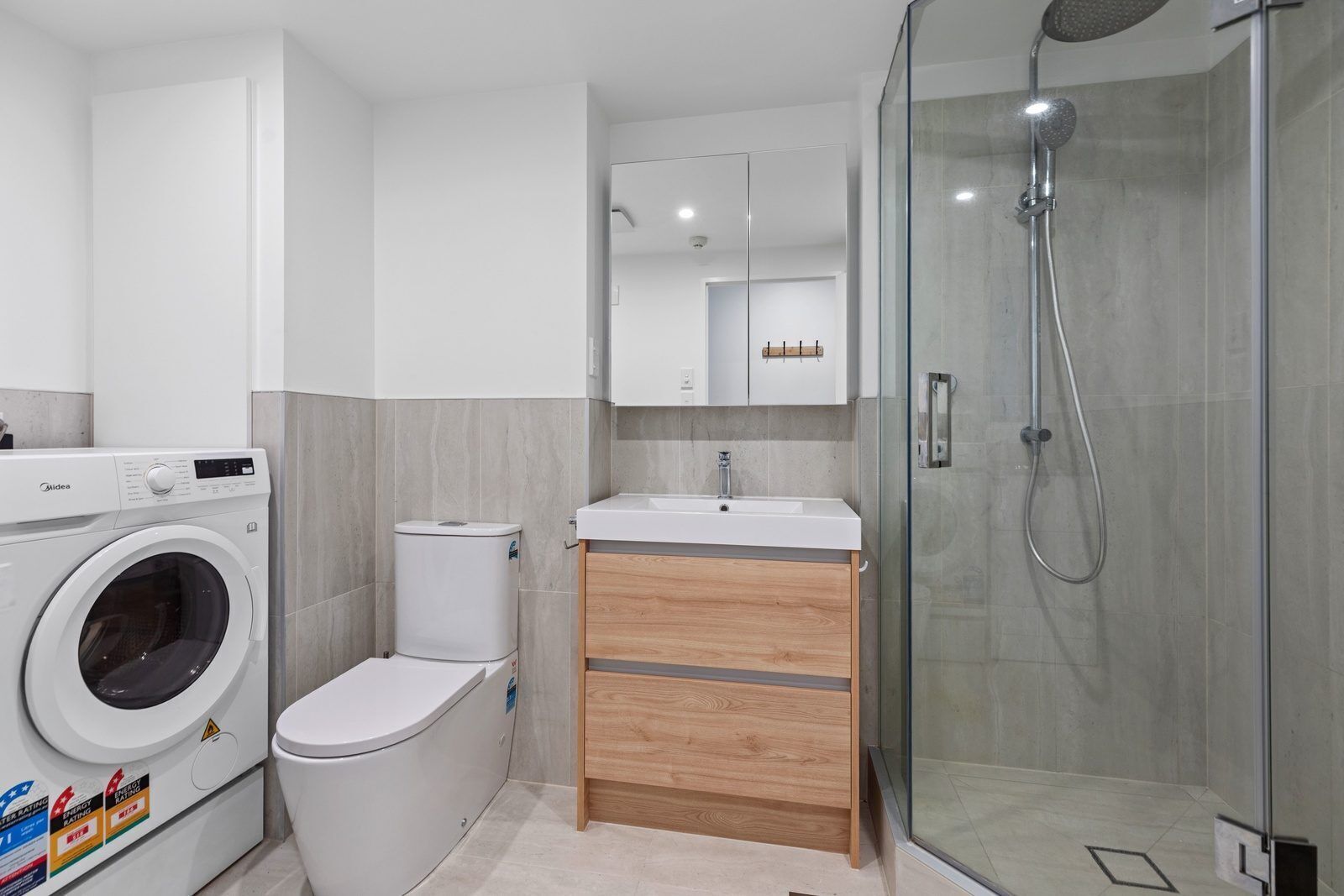 A modern bathroom with a washing machine, toilet, vanity, and glass-enclosed shower.