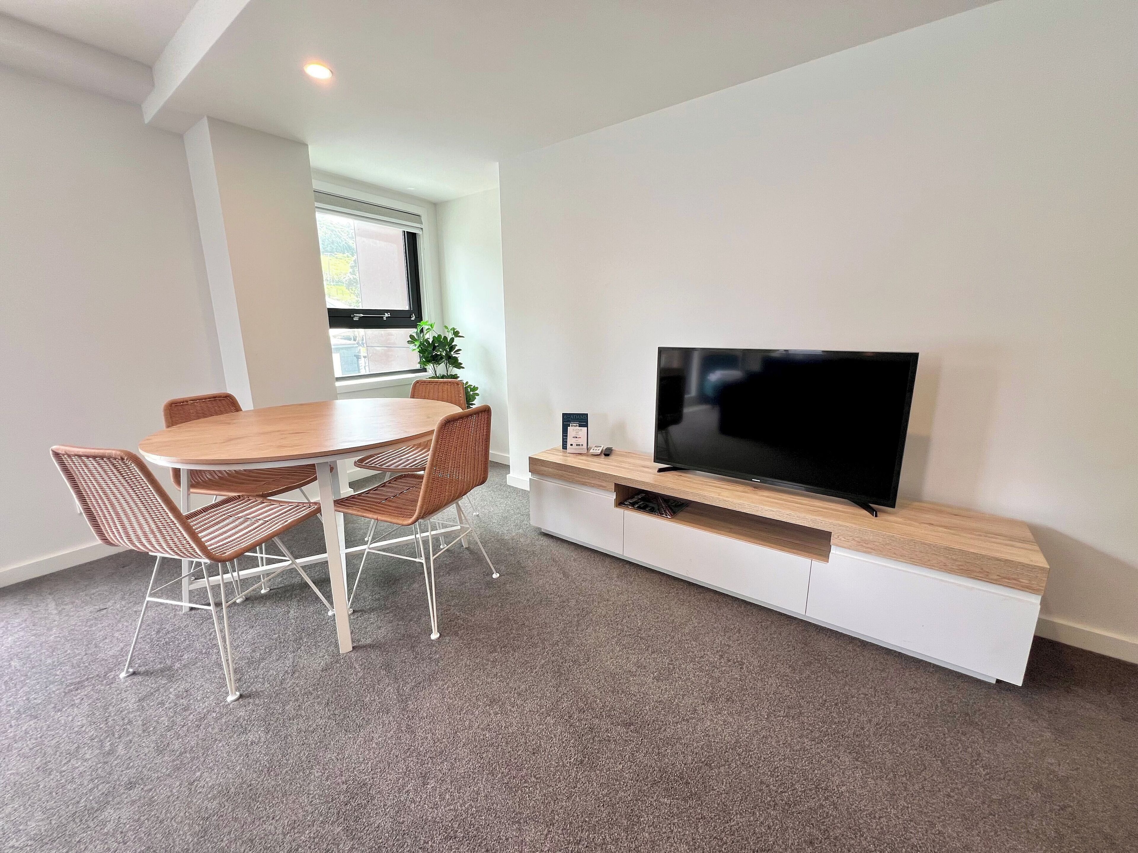 A modern living room with a dining area, a flat-screen TV on a wooden stand, and a potted plant.