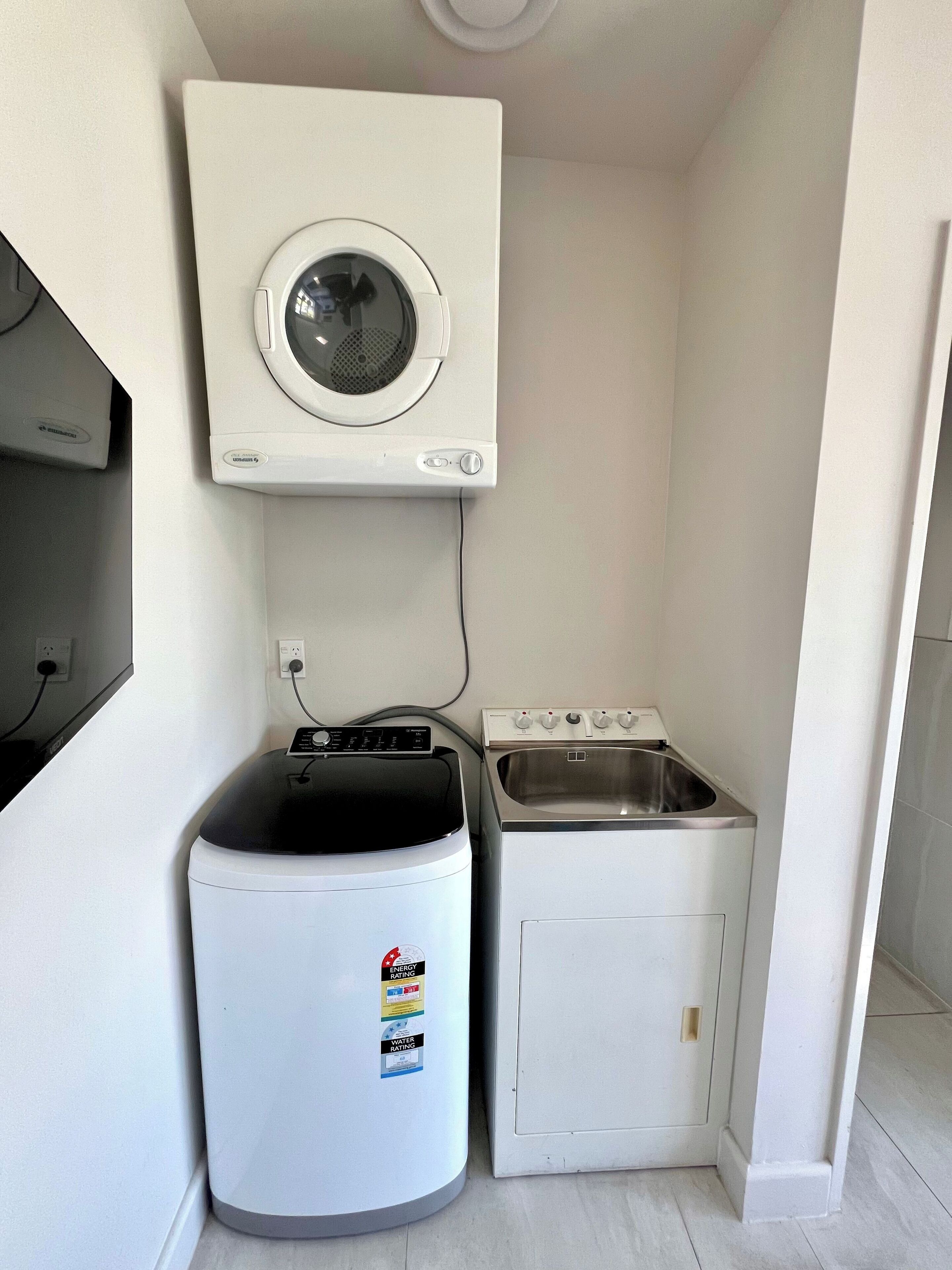 A compact laundry room with a wall-mounted washer and dryer, a small sink, and a cabinet.