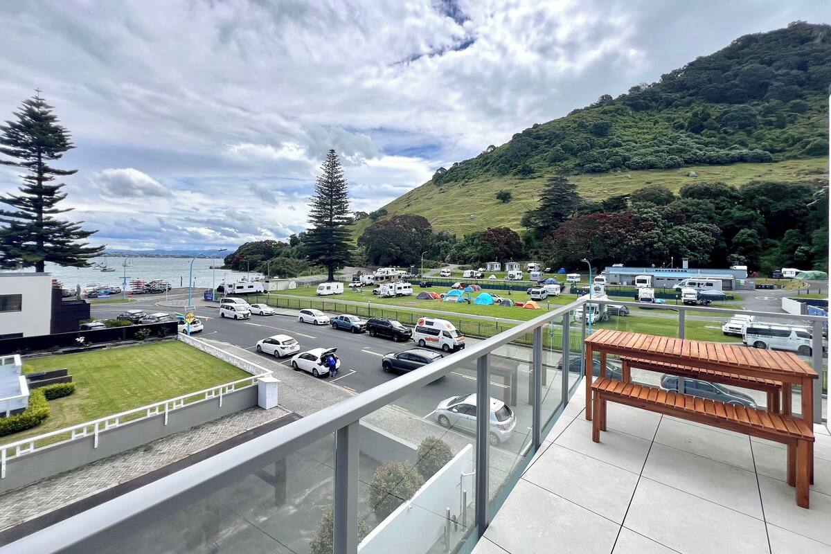 A view from a balcony overlooking a parking area with RVs and cars, a grassy area, and a hilly landscape with trees.