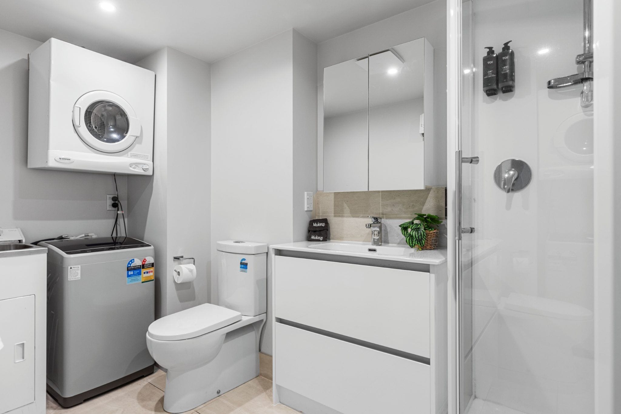 Uma casa de banho moderna com máquina de lavar roupa integrada, sanita e chuveiro.