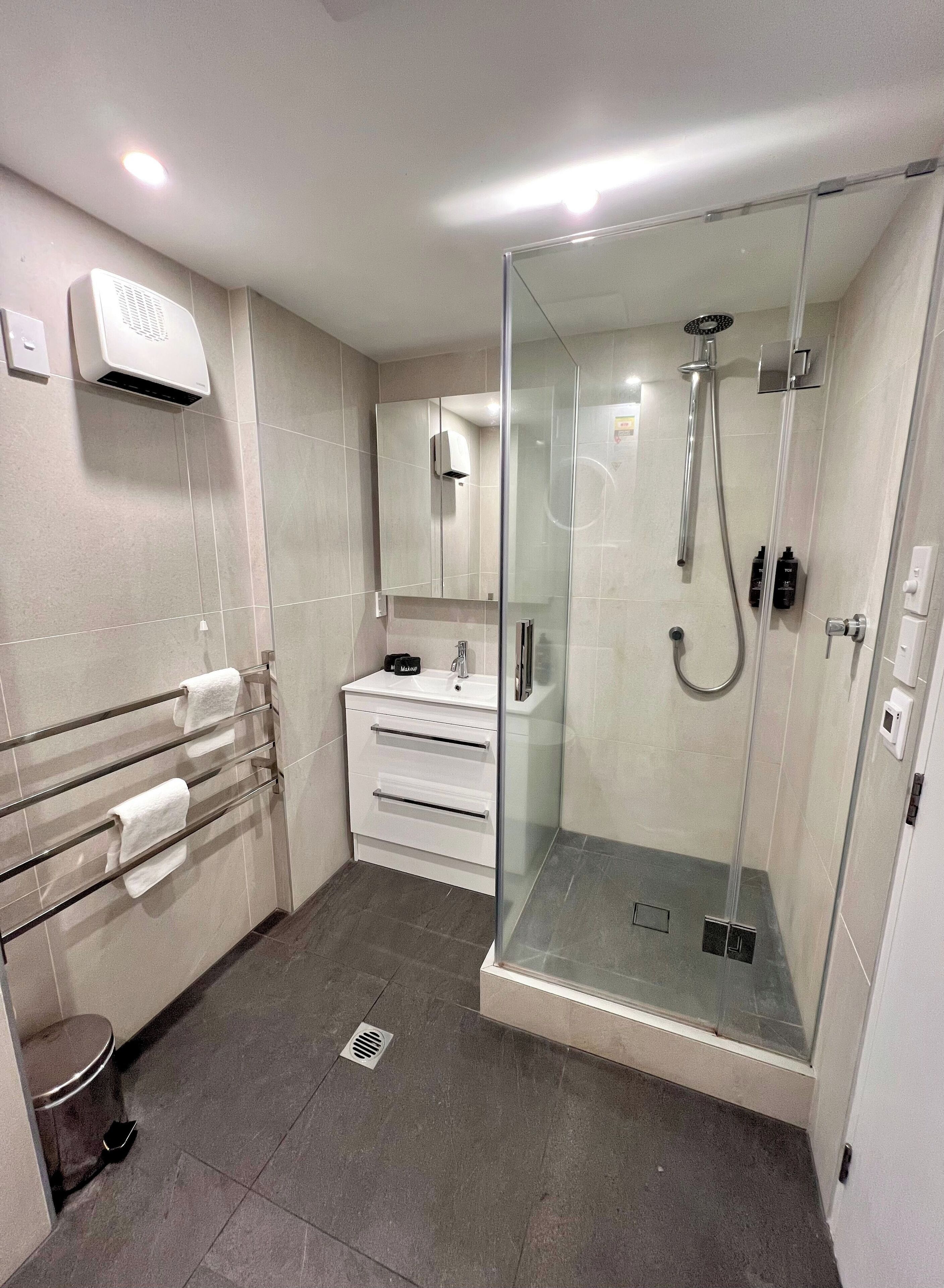 A modern bathroom with a glass-enclosed shower, a white vanity with a mirror, and a towel rack.