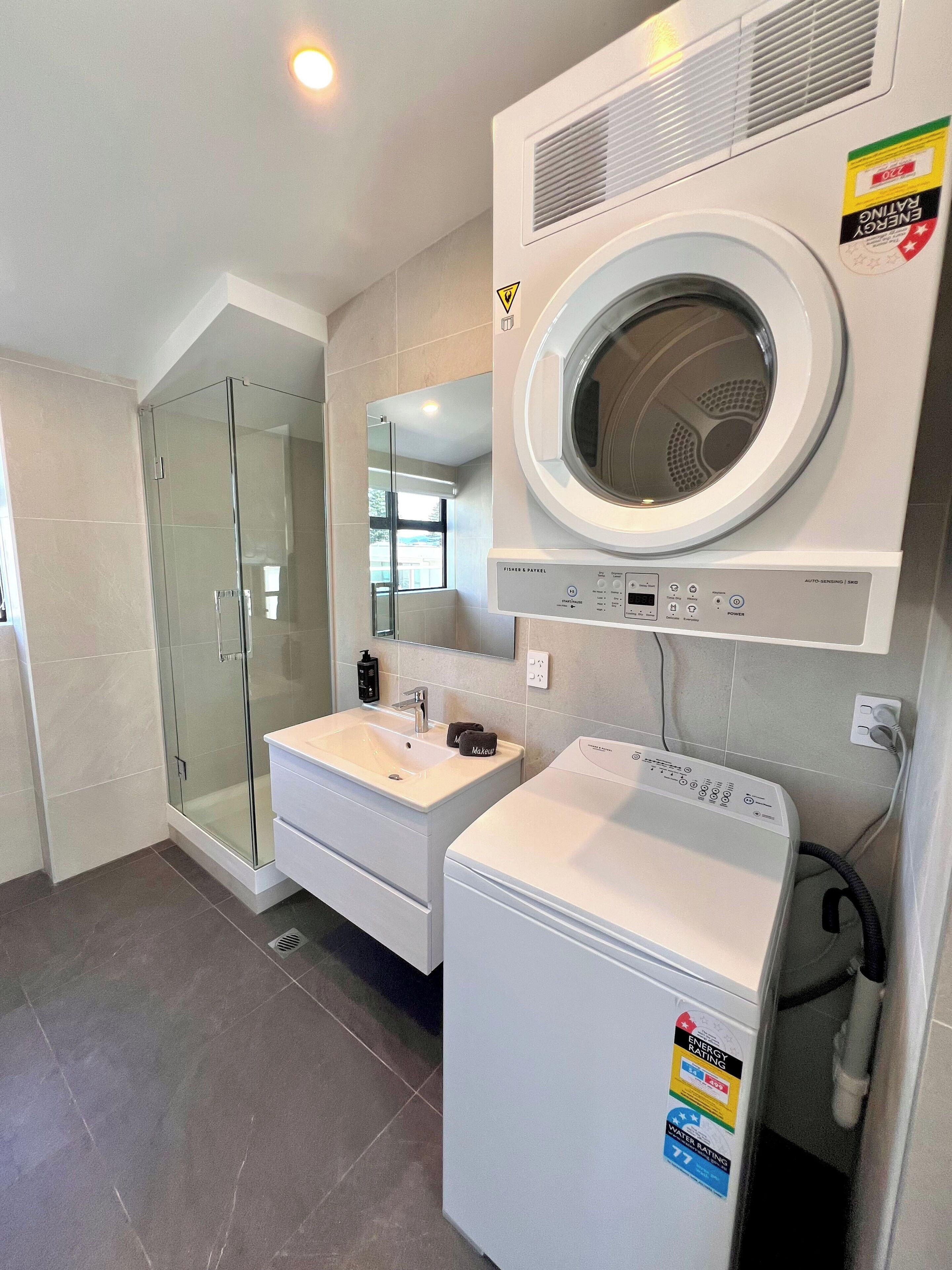Un baño moderno con cabina de ducha de vidrio, un lavabo con espejo y una lavadora de carga frontal.
