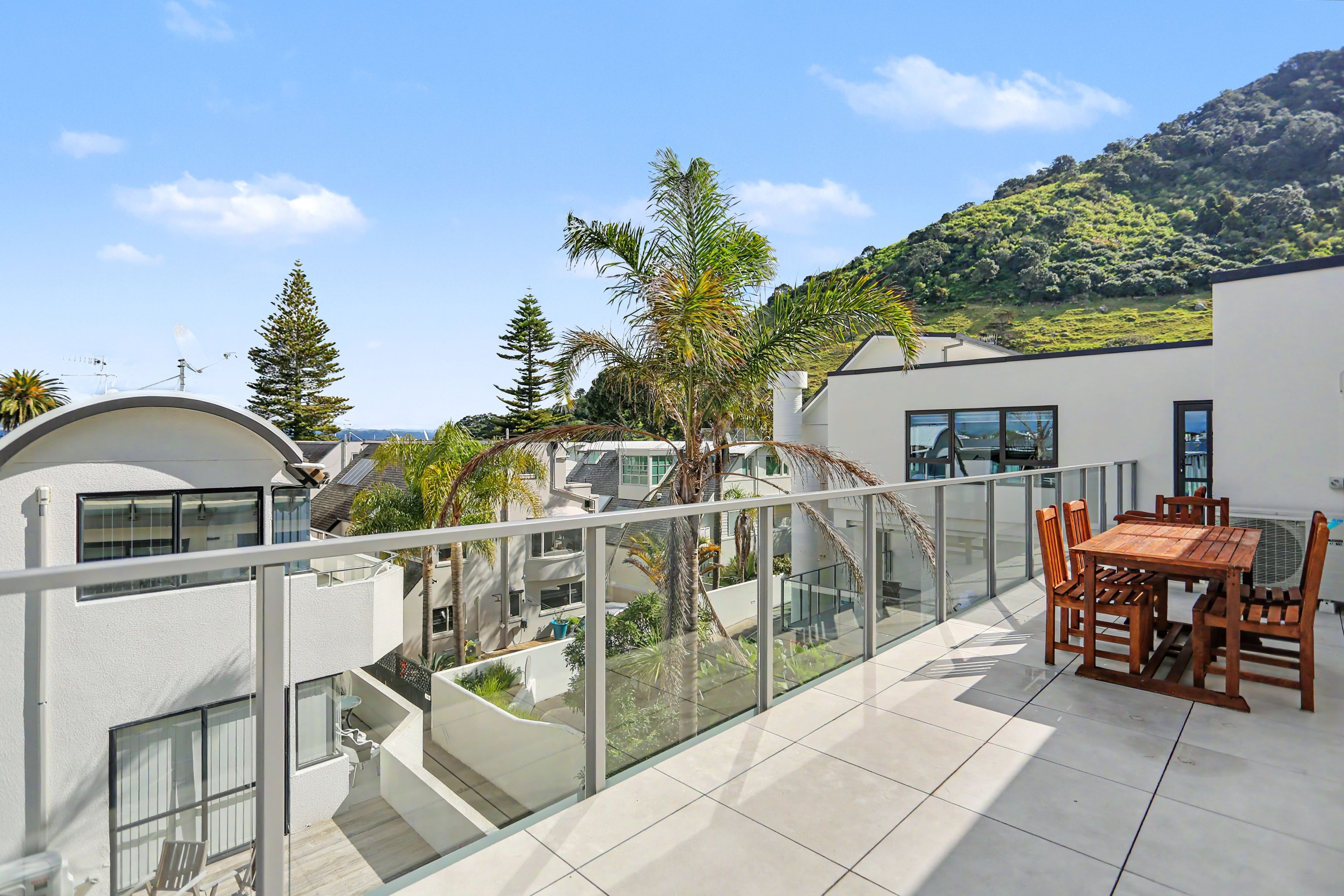 A modern residential building with a balcony, outdoor furniture, and a view of a hillside.