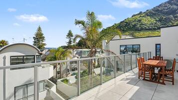 A modern residential building with a balcony, outdoor furniture, and a view of a hillside.