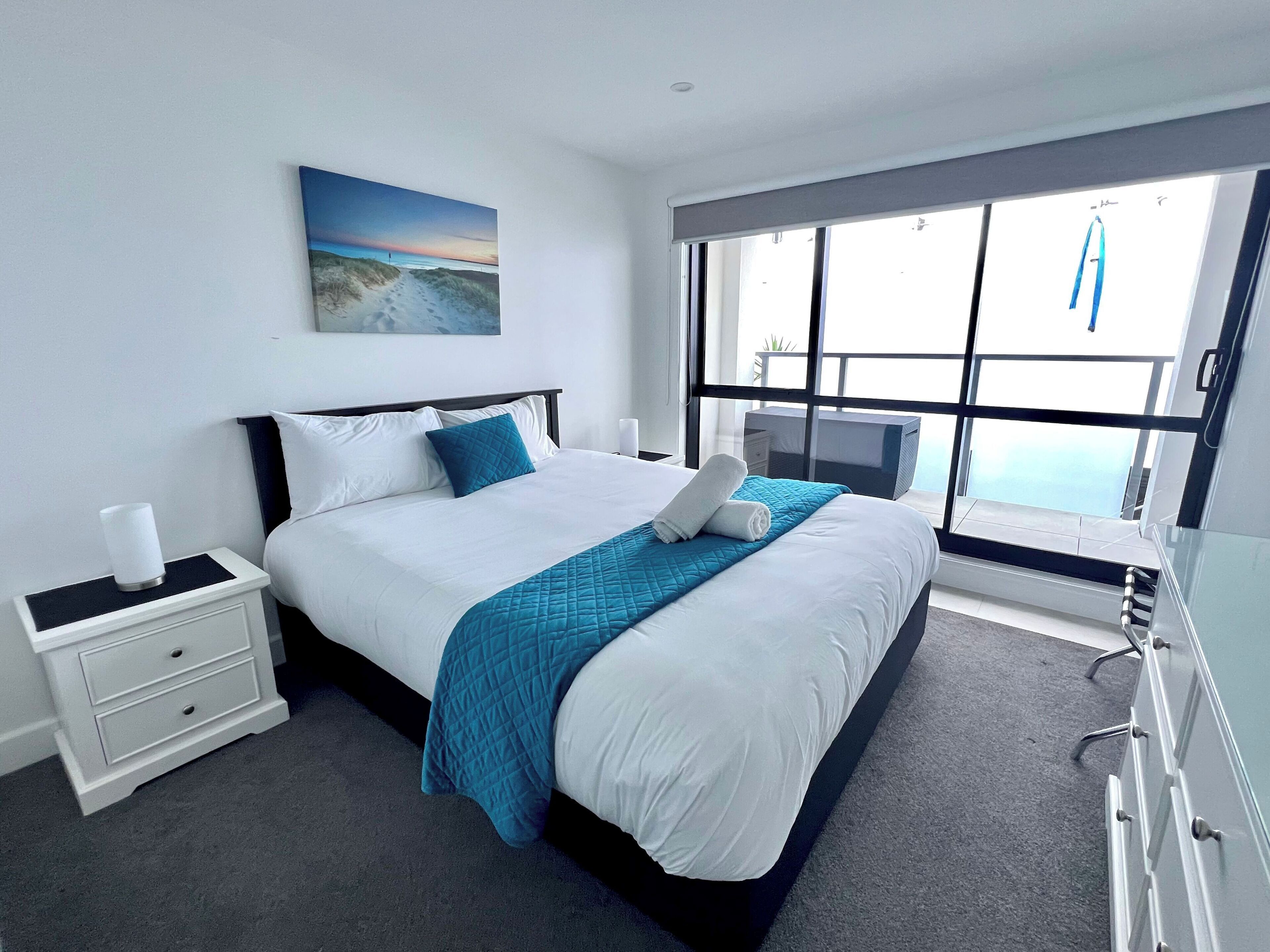 Une chambre à coucher moderne avec un grand lit, une table de chevet, une commode et une fenêtre donnant sur la mer.
