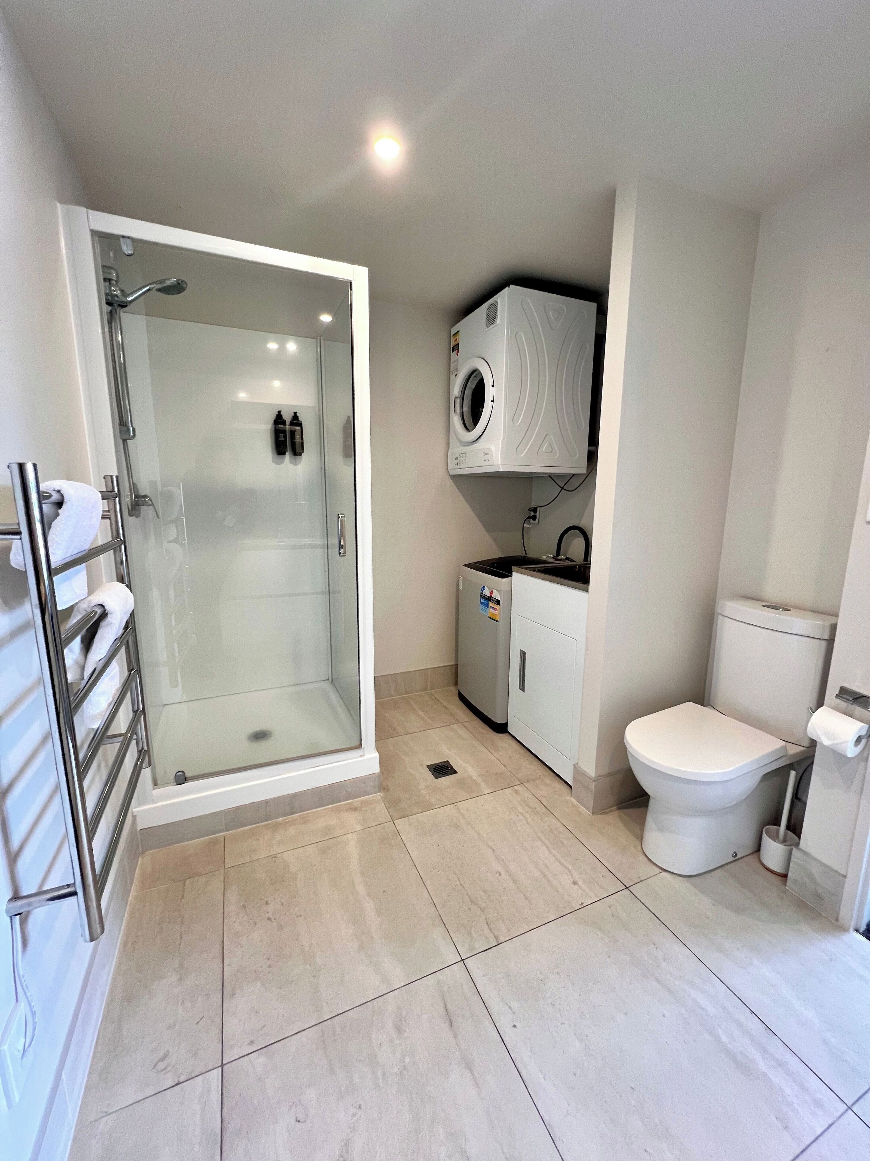 A modern bathroom with a glass-enclosed shower, a built-in washing machine, and a toilet.