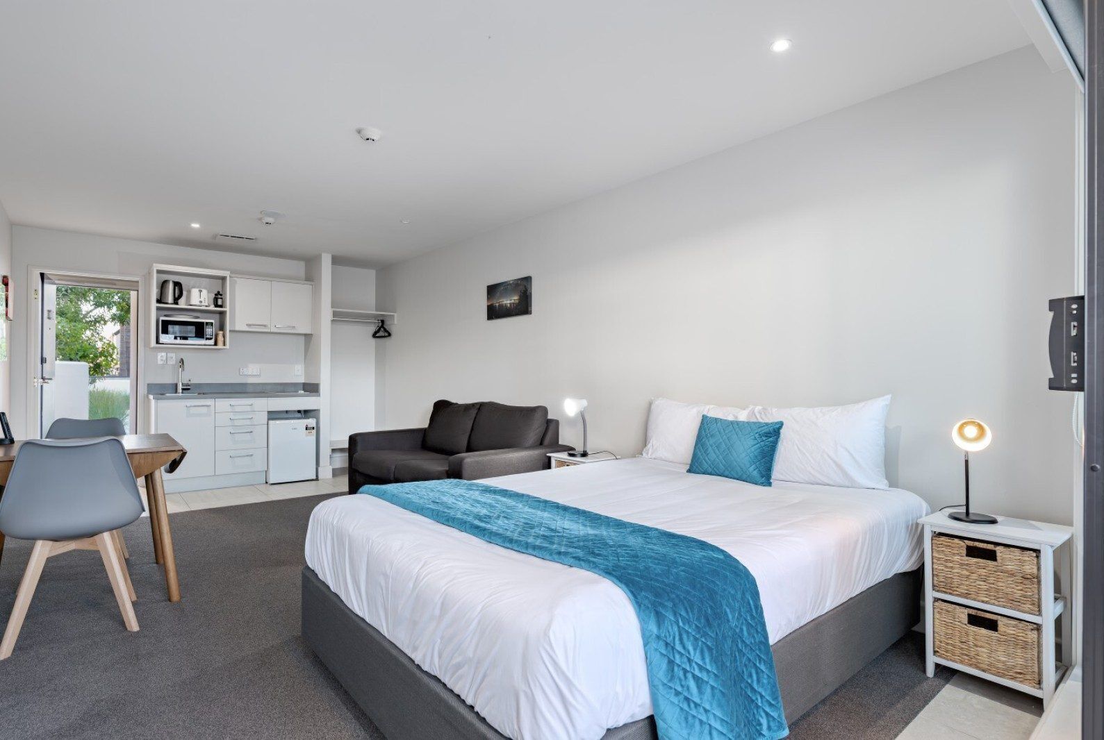 Une chambre d’hôtel moderne dotée d’un grand lit, d’un bureau, d’une chaise, d’une kitchenette et offrant une vue sur l’extérieur.