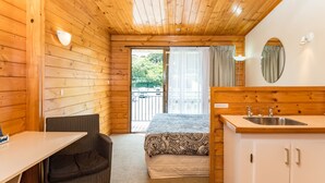 Een houten hutje met een bed, een tafeltje, een stoel, een wastafel en uitzicht op de omgeving.