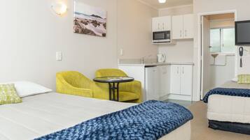 A hotel room with a bed, two yellow armchairs, a small table, a kitchenette with a microwave, and a TV.