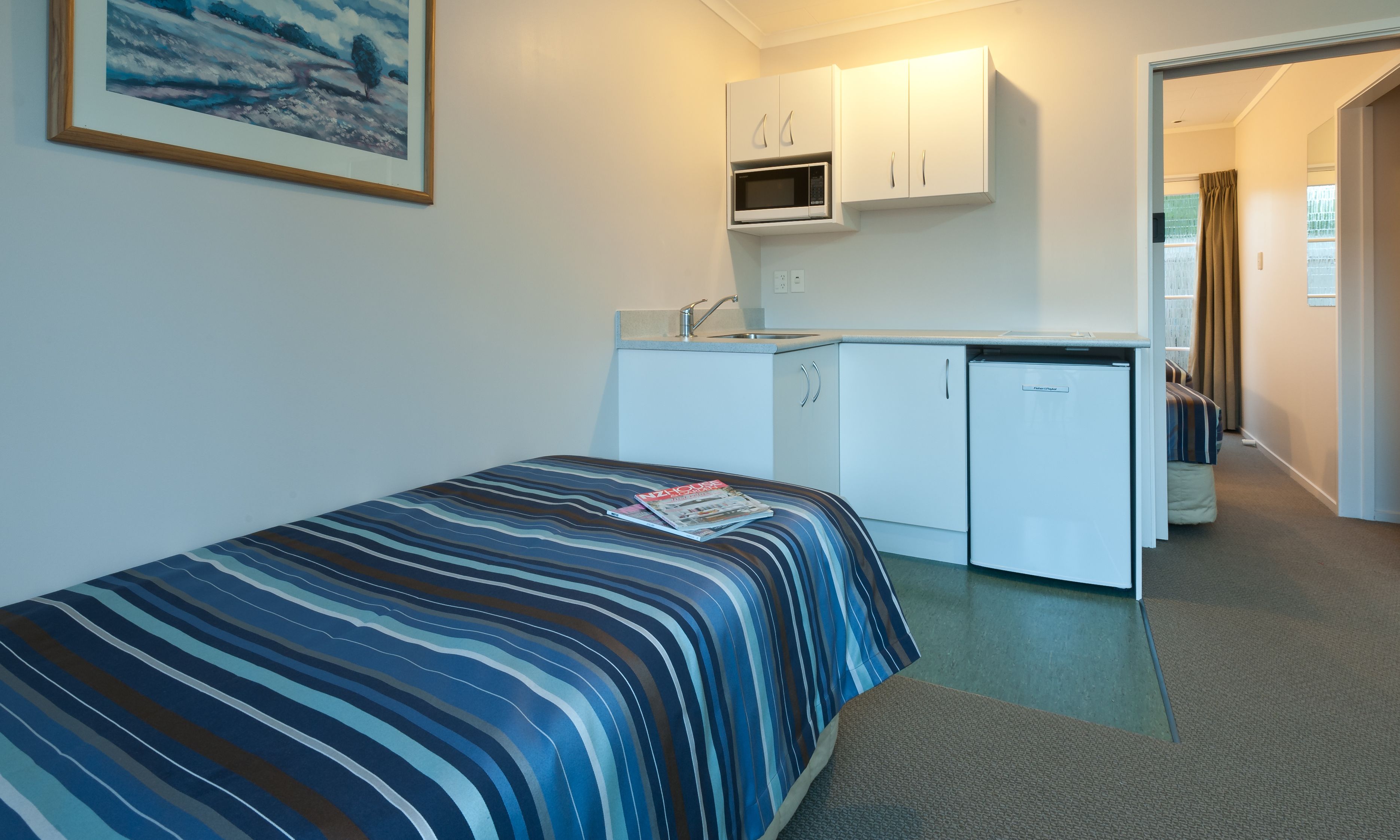 Una habitación de hotel compacta con una cama individual, kitchenette y baño visible a través de una puerta abierta.