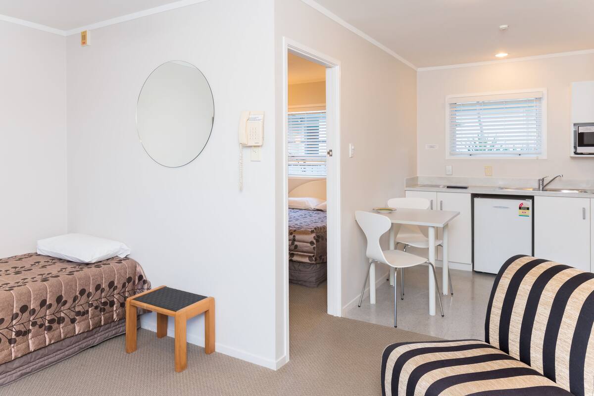 A compact room with a bed, a small table, a sofa, a kitchen area with a fridge, and a microwave.