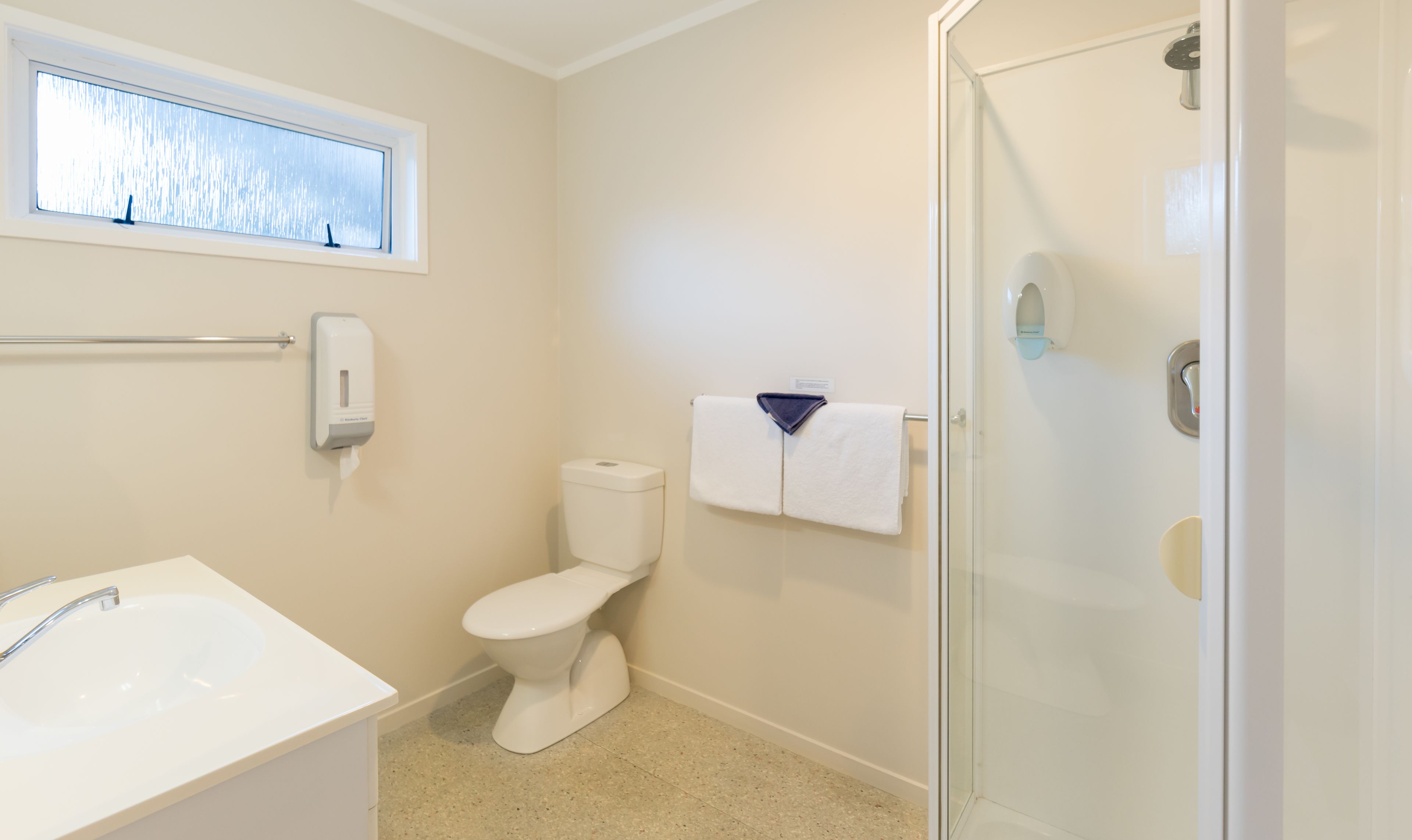 A bathroom with a toilet, a sink, a towel rack, and a glass shower enclosure.