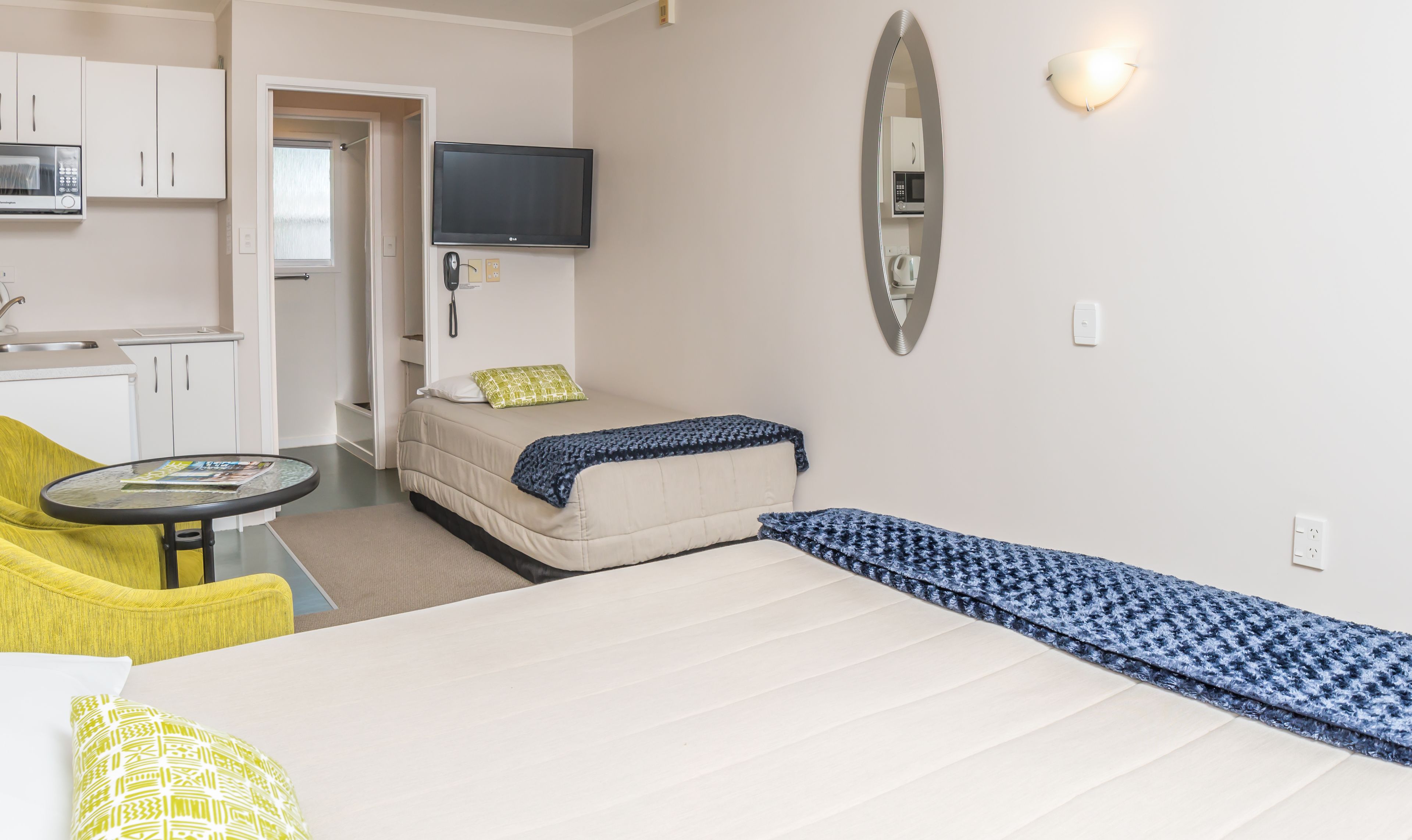 A hotel room with a bed, a sofa, a small table, a TV, and a kitchen area.