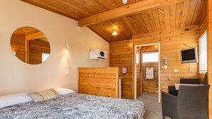 Een kamer met een bed, een ronde spiegel, een televisie en een rieten stoel.