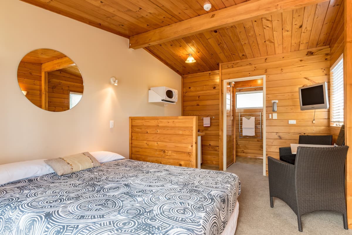 A room with a bed, a round mirror, a television, and a wicker chair.