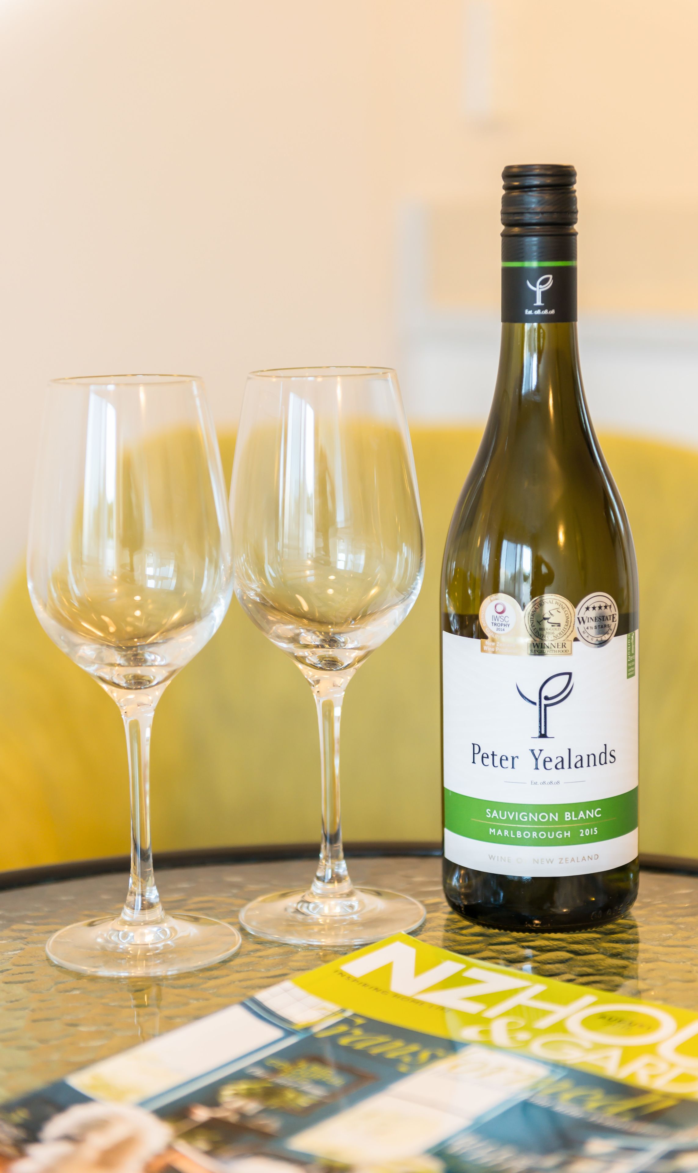 A bottle of Peter Yealands Sauvignon Blanc on a table with two empty wine glasses.