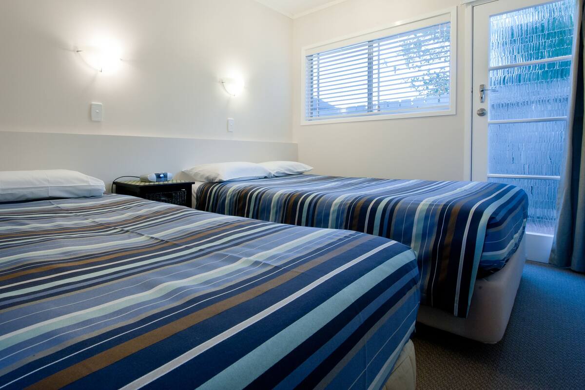 A hotel room with two beds, a nightstand, and a window with blinds.