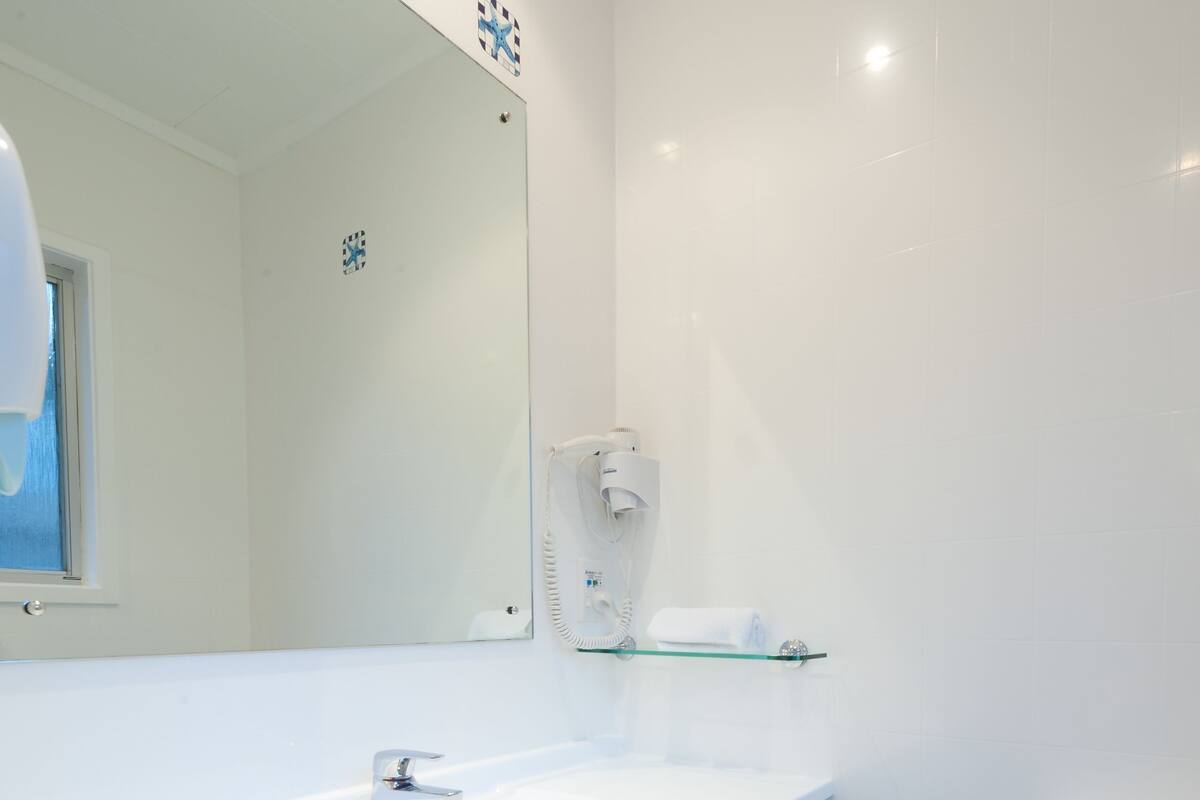 A bathroom with a white sink, a glass shelf, a mirror, and a toilet.