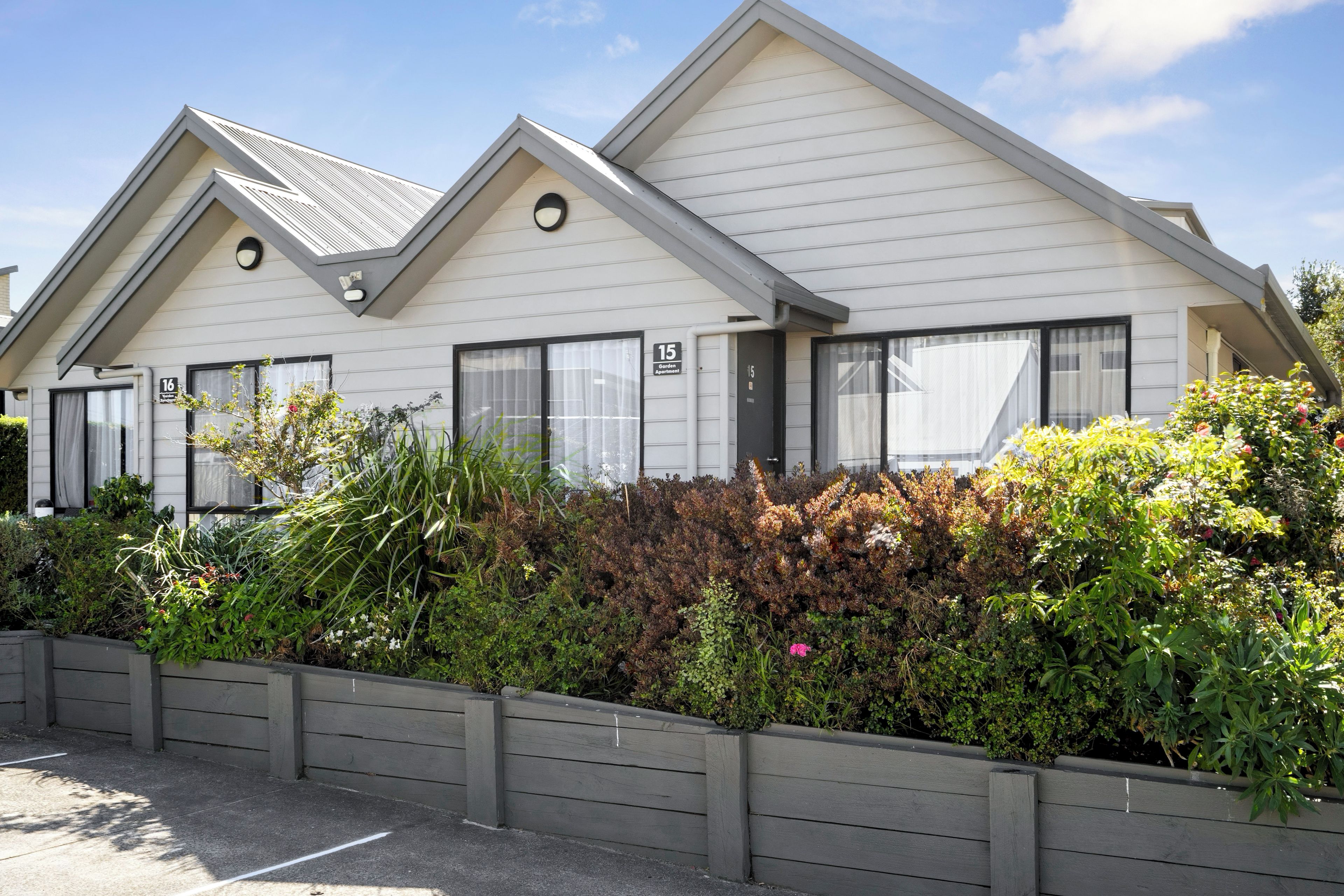 A row of modern, white-roofed buildings with numbered windows, surrounded by dense shrubbery.