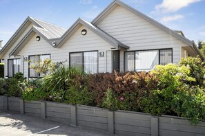 A row of modern, white-roofed buildings with numbered windows, surrounded by dense shrubbery.