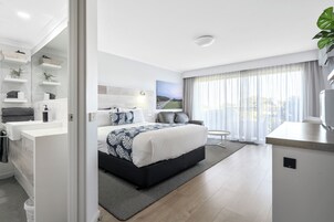 Una habitación de hotel moderna con una cama grande, una zona de estar, un baño con tocador y vistas al exterior a través de la ventana.