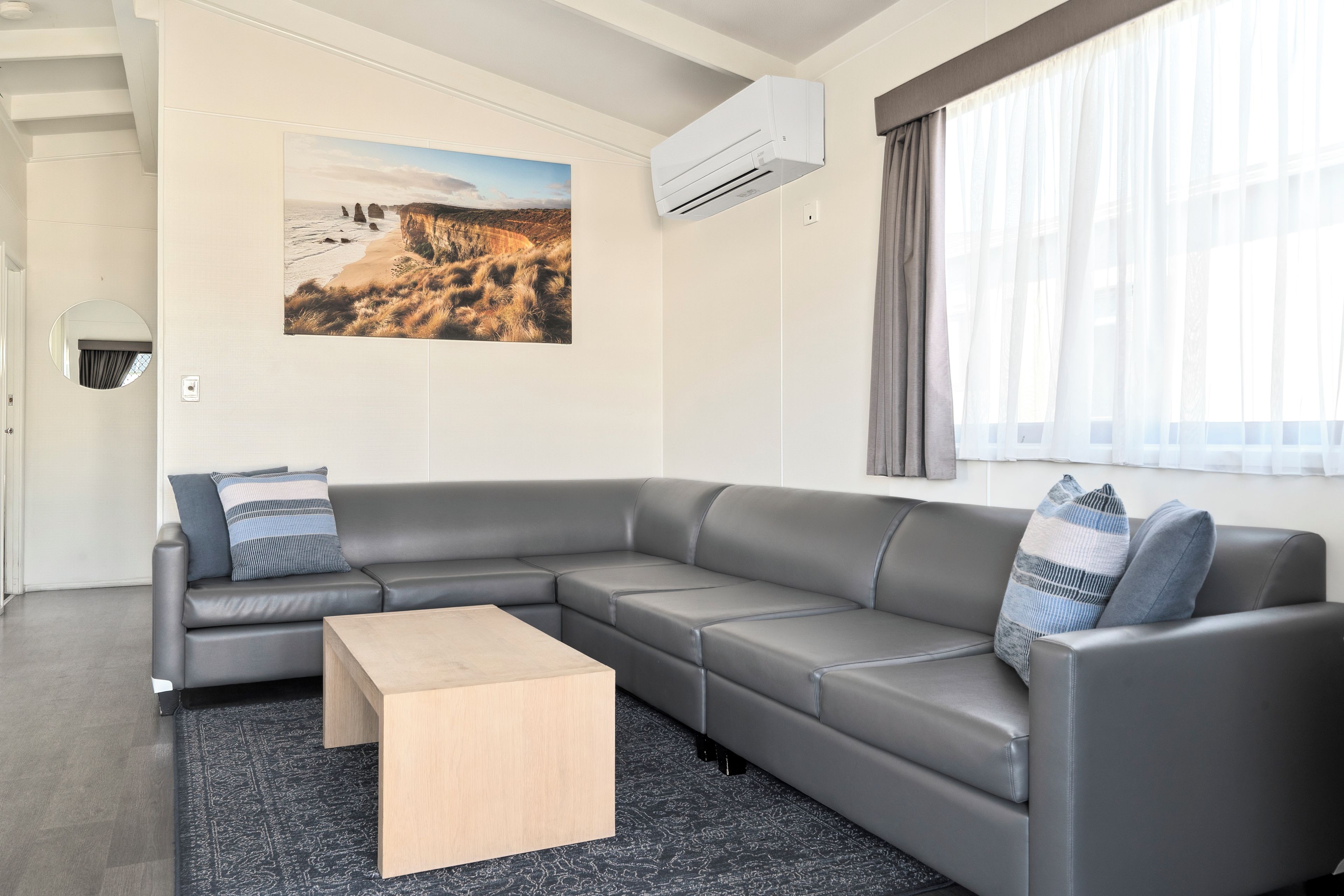 Ein modernes Wohnzimmer mit einem grauen Ecksofa, einem Holztisch und einem großen Landschaftsbild an der Wand.