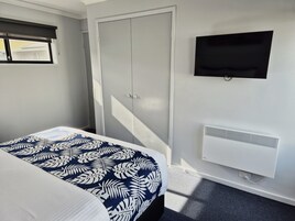 Una habitación de hotel con una cama, un armario, un televisor y un aire acondicionado instalado en la pared.