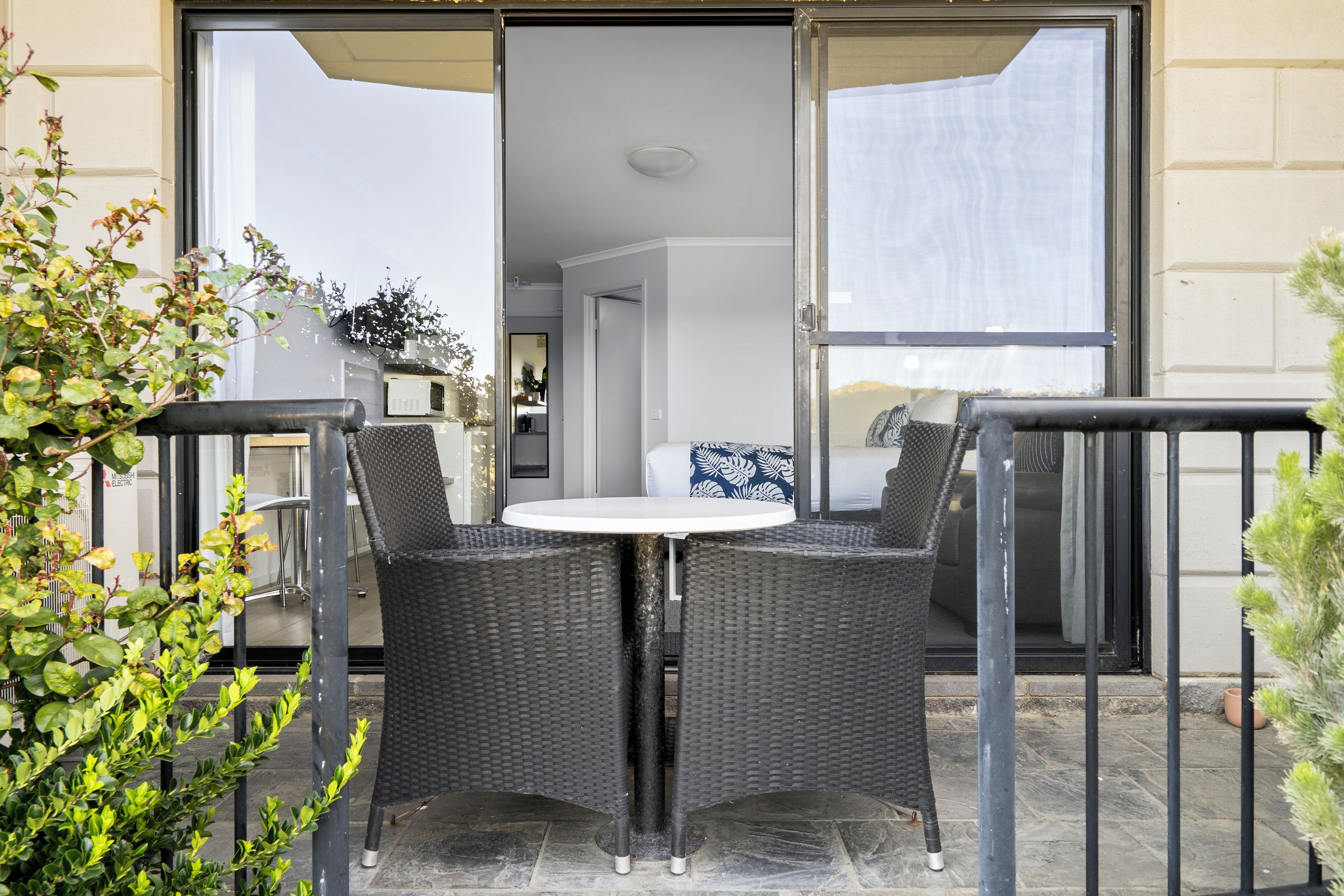 An outdoor seating area with a table and chairs, a sliding glass door leading to a kitchen, and a view of the street.
