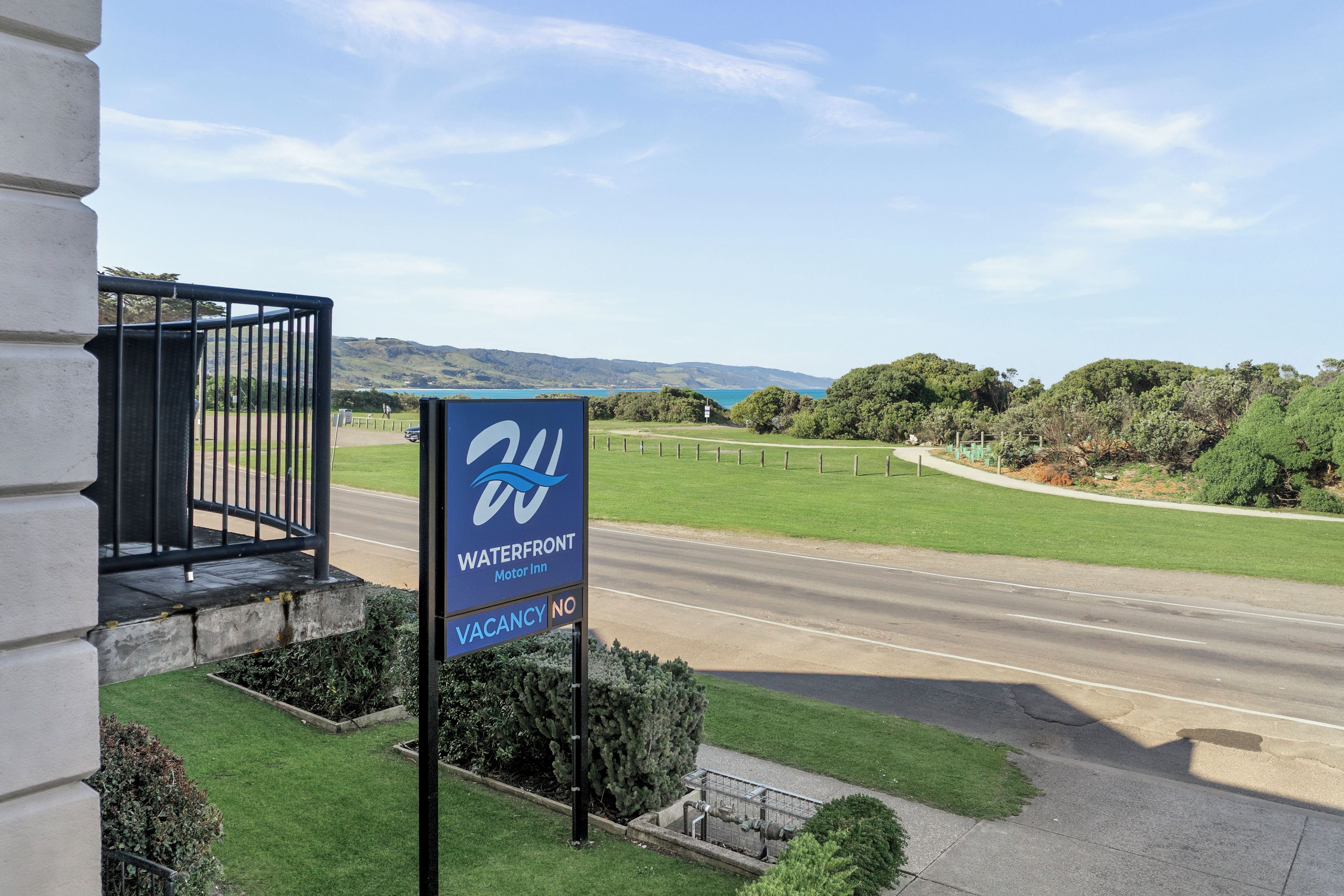 A sign for a Waterfront Motor Inn with a view of a road and greenery.