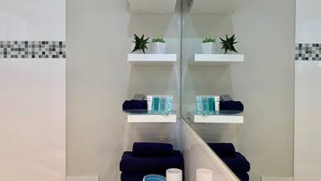 Bathroom features a large mirror, white tiled walls, and a countertop with toiletries and towels.
